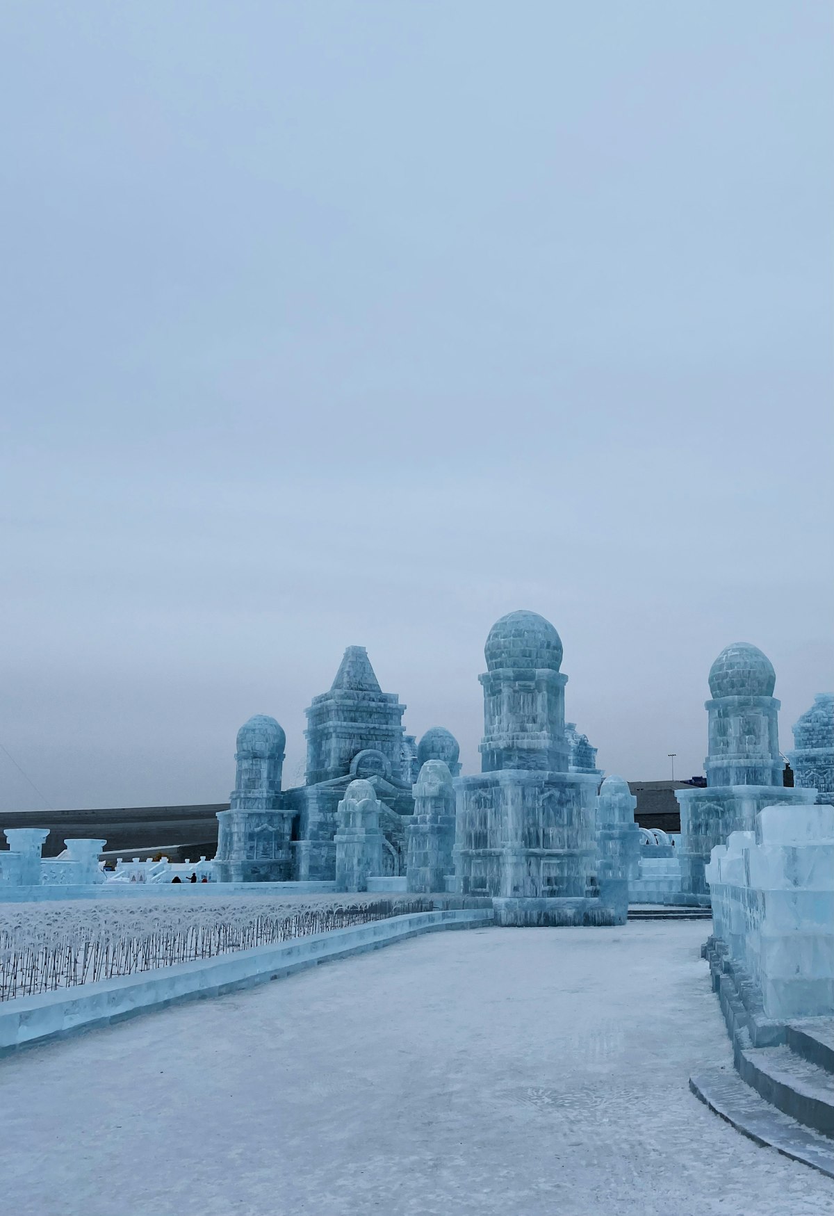 Massive illuminated ice sculpture at Harbin Ice and Snow World with clock tower in background